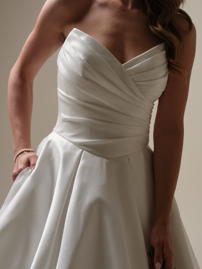 Aubrielle by Maggie Sottero — close-up of a strapless sweetheart ruched bodice on a structured satin ballgown wedding dress, paired with a full pleated skirt in a studio setting.