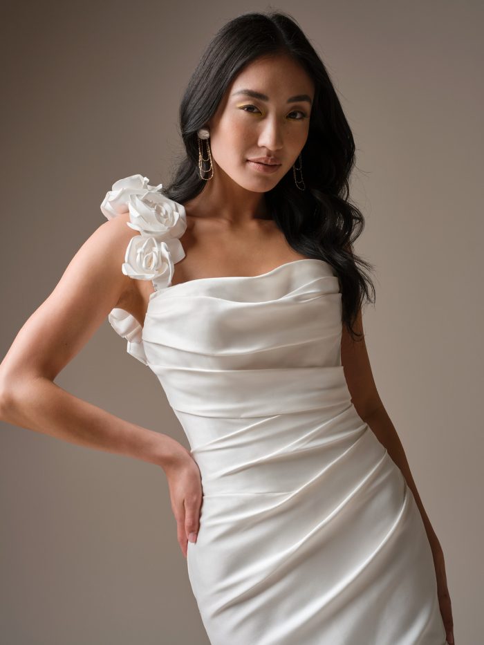 One-shoulder satin wedding dress Emelina by Maggie Sottero featuring draped bodice and sculpted floral shoulder detail.
