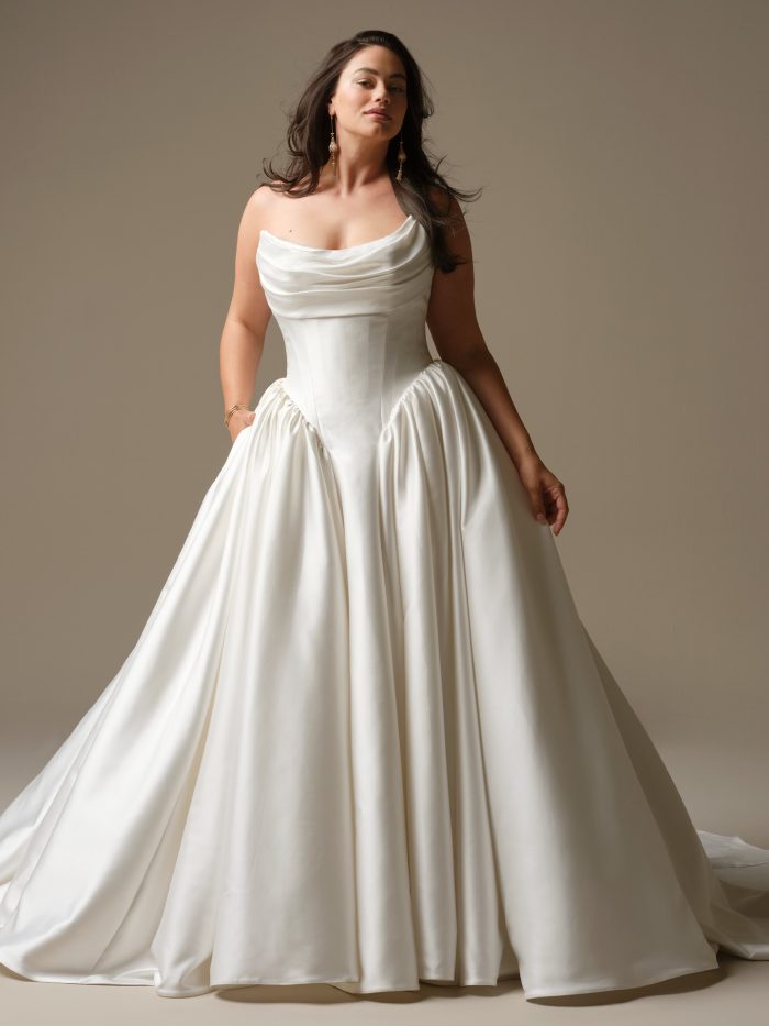 Model wearing the Hudson ball gown wedding dress by Maggie Sottero, featuring a draped scoop neckline, structured corset bodice, and full satin skirt with dramatic volume.