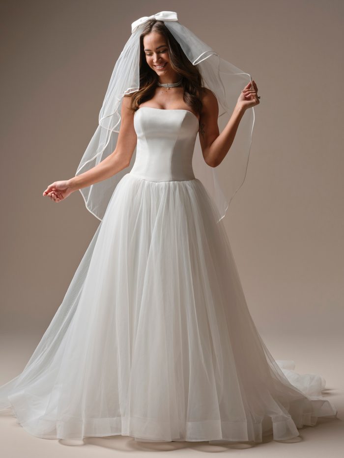 Bride wearing the Hudson veil by Maggie Sottero, featuring a soft fingertip design with a bow detail, paired with a strapless gown and full tulle skirt.