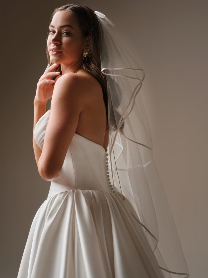 Back and side view of a bride in the Hudson veil by Maggie Sottero, highlighting the bow accent, soft fingertip length, and delicate trim paired with a strapless bridal gown.