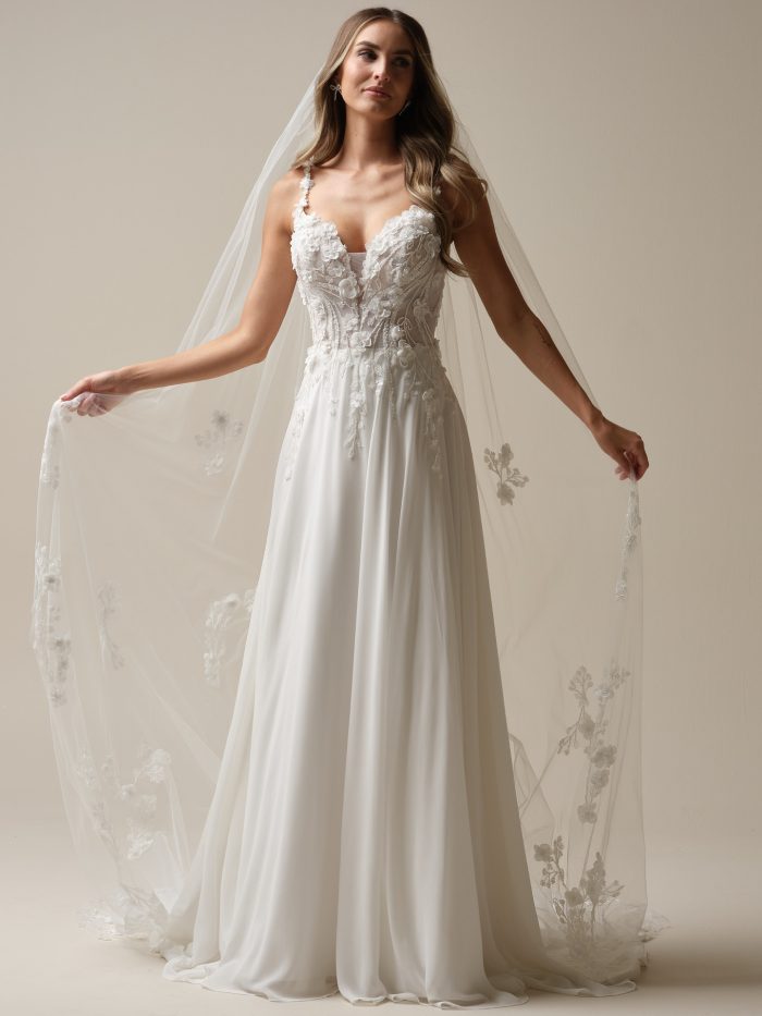 Bride wearing the Hunter A-line wedding dress by Maggie Sottero, featuring a plunging V-neckline, sheer floral lace bodice with 3-D flower details, and a flowing chiffon skirt with a light, airy silhouette.