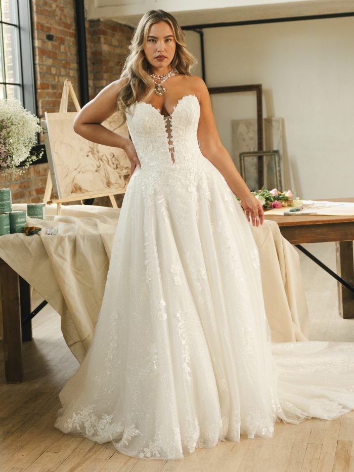 Bride wearing a strapless ballgown wedding dress with a plunging sweetheart neckline, lace bodice, and glitter tulle skirt. The gown features floral lace appliqués and a chapel-length train, creating a romantic and glamorous bridal look.