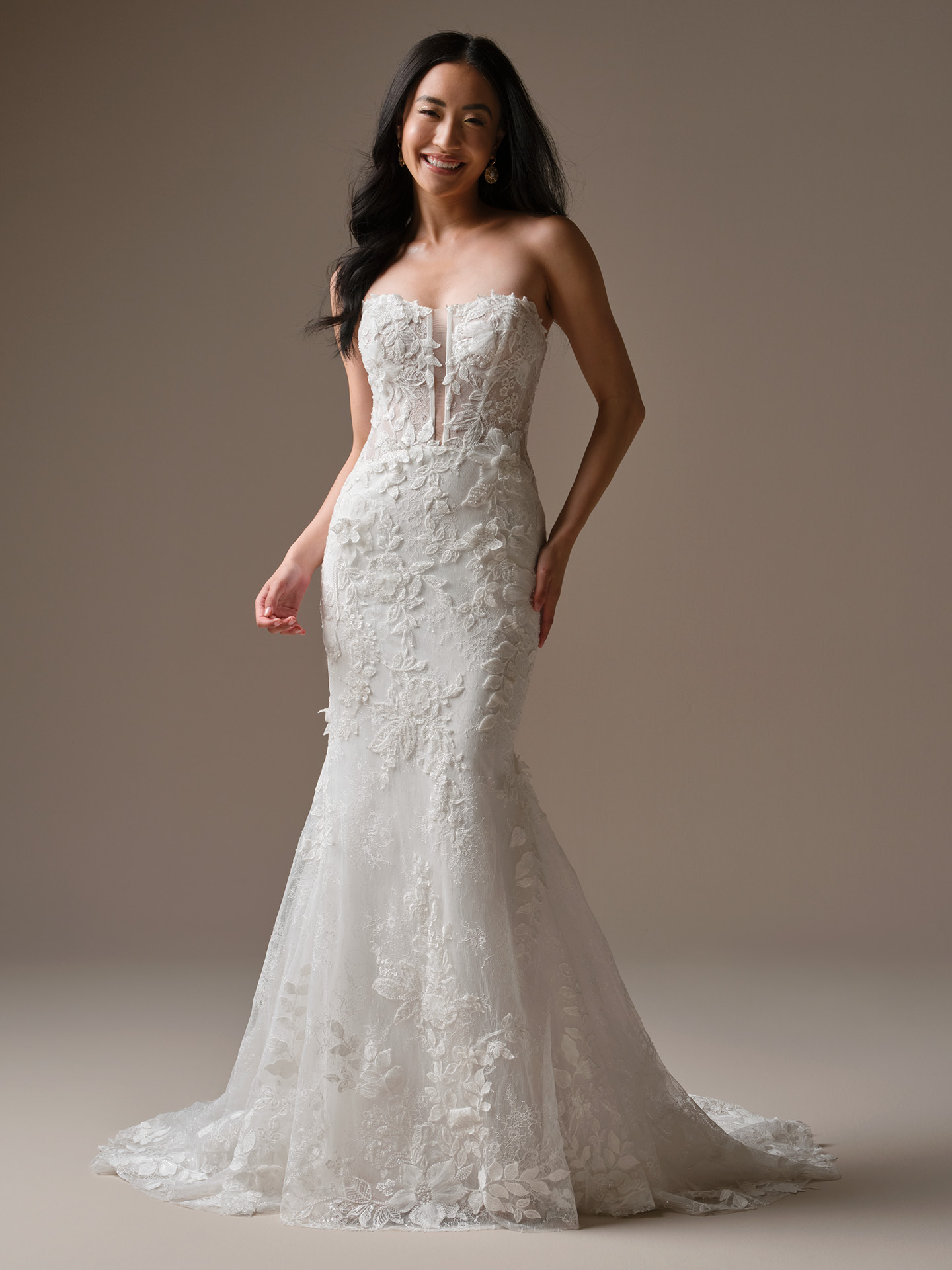 Bride wearing Laurie by Maggie Sottero, a strapless lace fit-and-flare wedding dress featuring a plunging illusion neckline, dimensional floral lace appliqués, fitted silhouette, and a soft lace train.