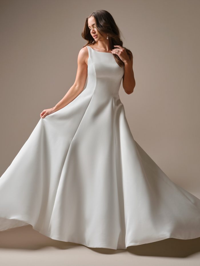 Model wearing the Lawrence A-line wedding dress, featuring a sleek high bateau neckline, clean satin construction, and a full flowing skirt for a modern minimalist bridal look.