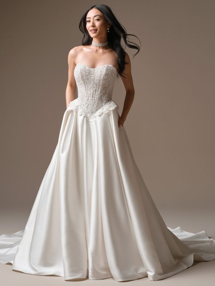 Full-length view of the London ballgown wedding dress by Maggie Sottero featuring a strapless pearl-embellished bodice and a full satin skirt with a soft train.