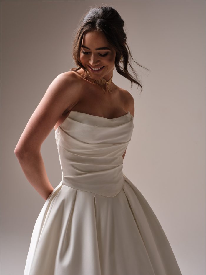 Close-up of the Maureen by Maggie Sottero strapless ballgown wedding dress highlighting the draped bodice, smooth satin fabric, and full skirt with pockets.