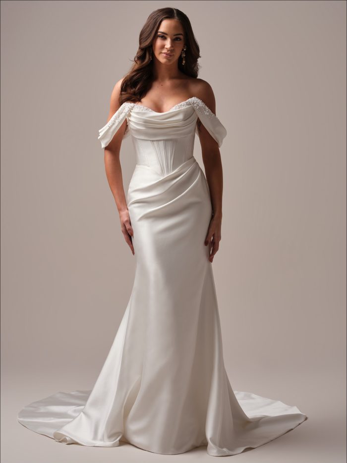 Bride wearing the Melissa fit and flare wedding dress with beaded off the shoulder straps, a draped sweetheart bodice, and a sleek satin skirt with a soft train.