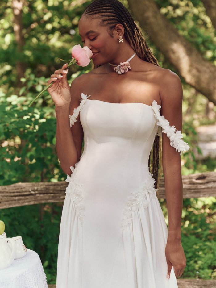 Close-up of the Morwenna wedding dress by Maggie Sottero, highlighting the smooth satin bodice, delicate 3-D floral off-the-shoulder straps, and romantic boho styling with soft florals.