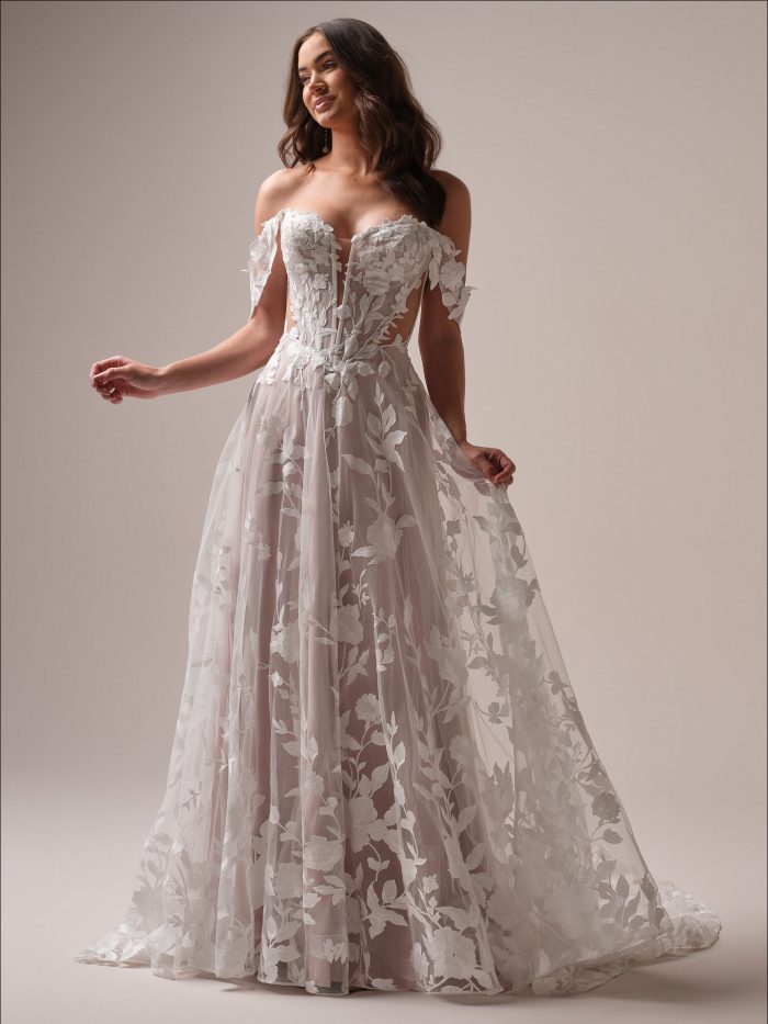 Bride wearing the Natalie A line wedding dress featuring off the shoulder lace motifs, a plunging illusion bodice, and a flowing floral tulle skirt.