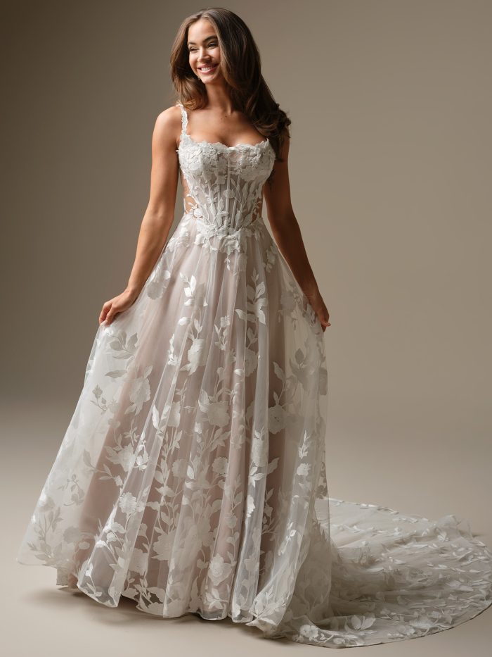 Bride wearing the Natalie Marie A-line wedding dress by Maggie Sottero, featuring a floral lace bodice with exposed corsetry, delicate lace straps, and a flowing embroidered tulle skirt with botanical motifs.