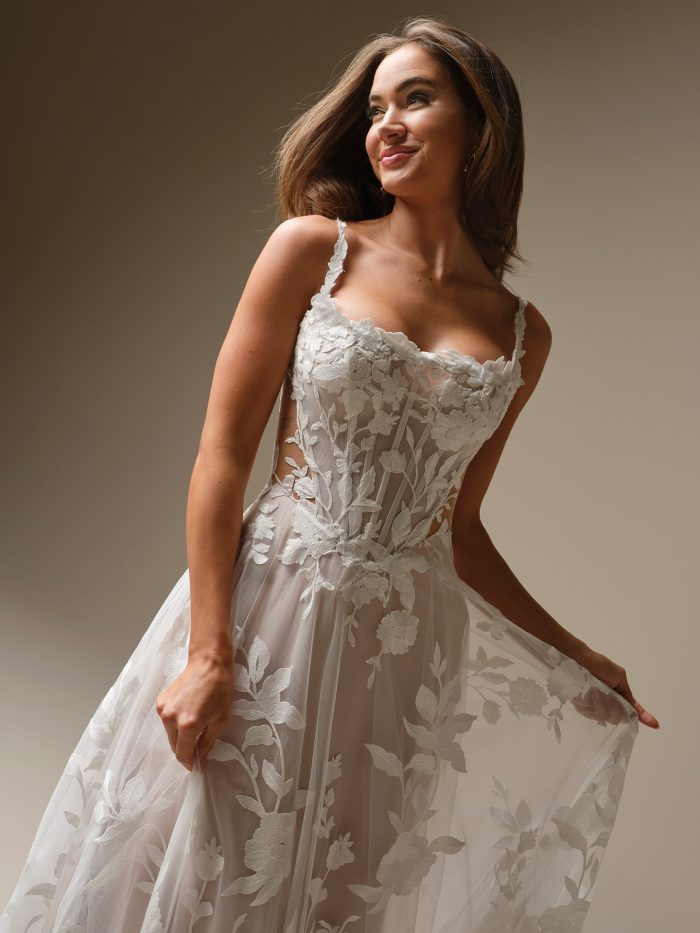 Close-up of the Natalie Marie wedding gown by Maggie Sottero, showcasing the floral lace bodice, delicate straps, sheer side panels, and embroidered tulle skirt for a romantic, ethereal bridal look.