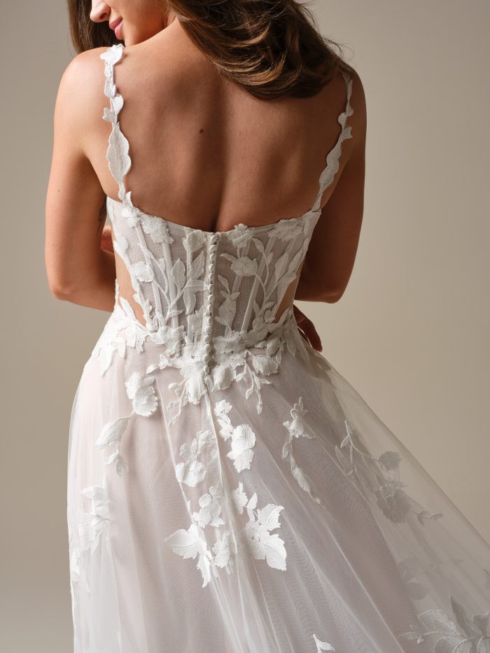 Back view of the Natalie Marie boho A-line wedding dress featuring a sheer lace corset bodice with floral appliqués, button-back closure, and an airy tulle skirt.