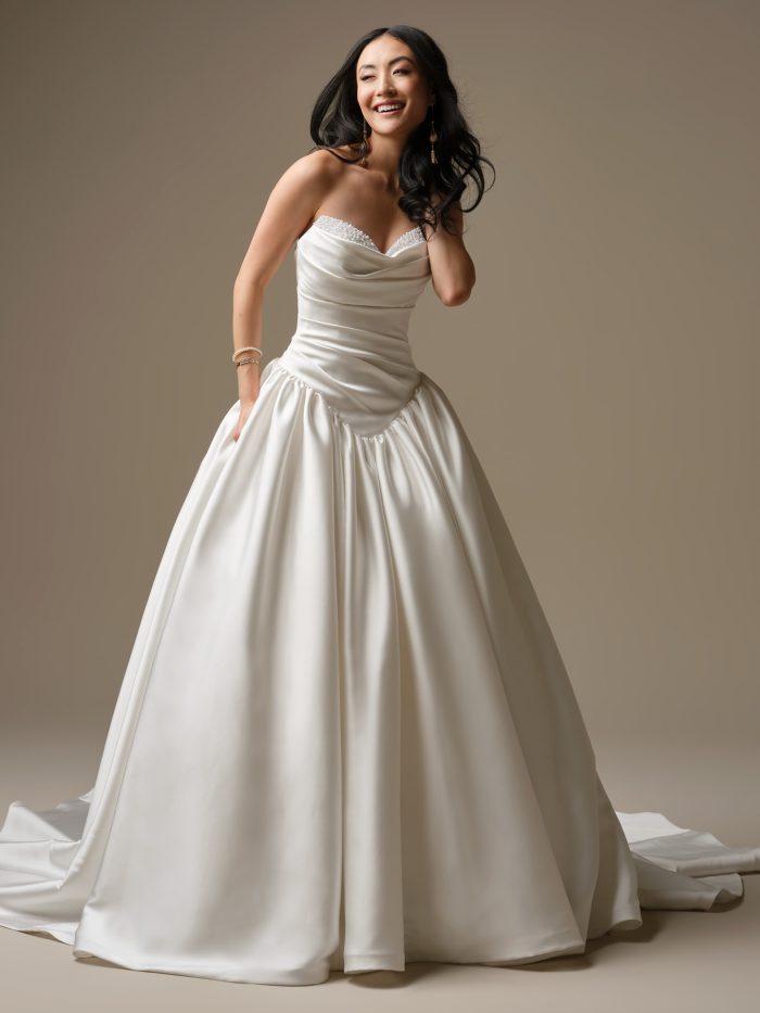 Pasadena satin ballgown featuring an asymmetrically draped bodice, exaggerated basque waistline, strapless sweetheart neckline with bead and pearl accents, and pockets.