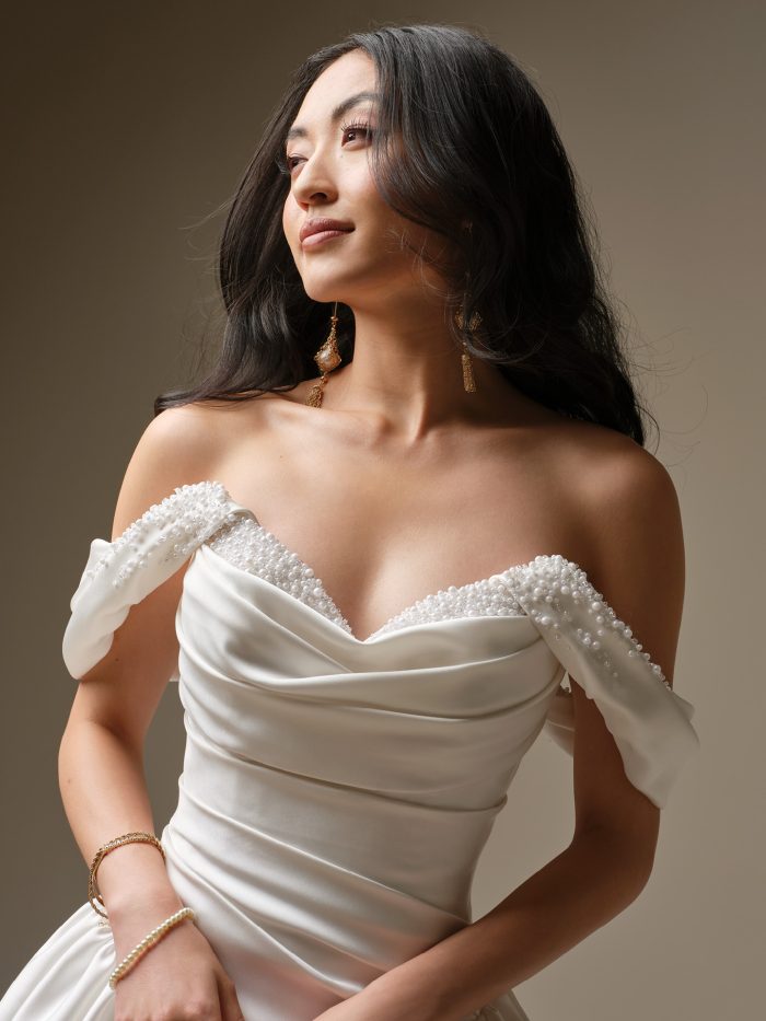 Close-up of the Pasadena wedding dress by Maggie Sottero featuring an off-the-shoulder pearl-embellished neckline and softly draped satin bodice.