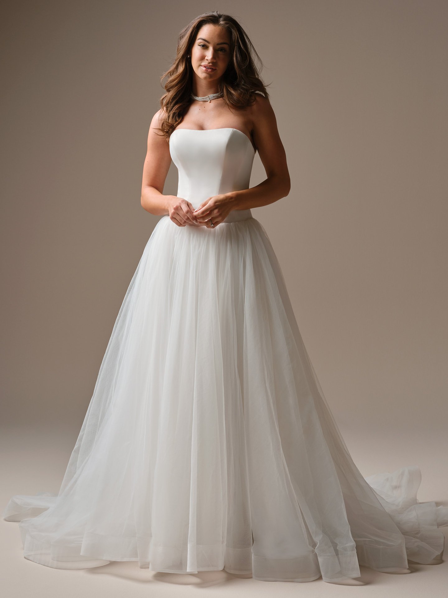 Alt text: Bride wearing Shirley by Maggie Sottero, a strapless ballgown wedding dress featuring a smooth fitted bodice and a soft layered tulle skirt with a romantic flowing train.