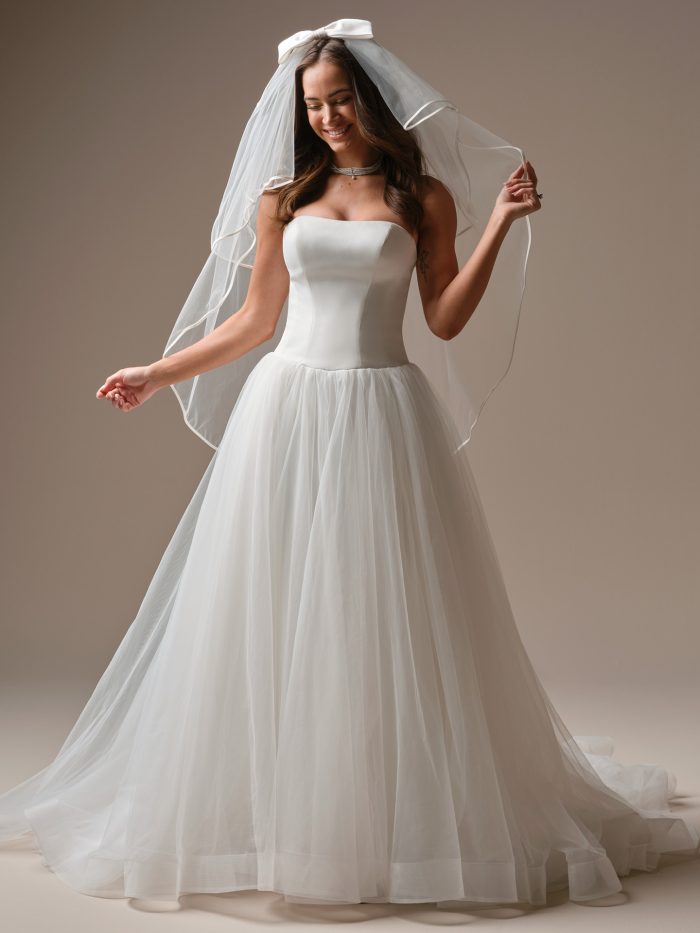 Shirley by Maggie Sottero strapless drop-waist wedding dress with a structured bodice and flowing tulle skirt, styled with a soft bridal veil