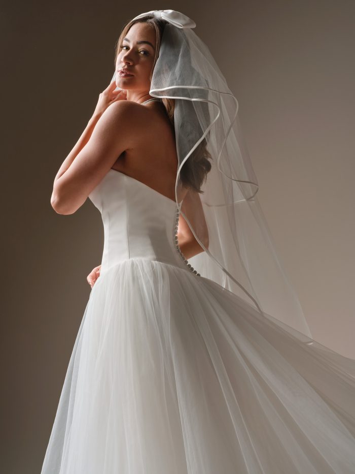 Back view of the Shirley ball gown wedding dress showing the smooth satin bodice, covered buttons down the back, and the airy tulle skirt flowing behind the bride beneath a bow-accented veil.