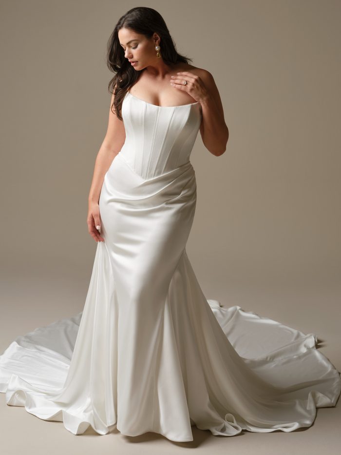 A model wearing the Maggie Sottero Sinclaire wedding dress, featuring a structured strapless bodice with visible boning and a sleek satin fit-and-flare skirt with soft draping.