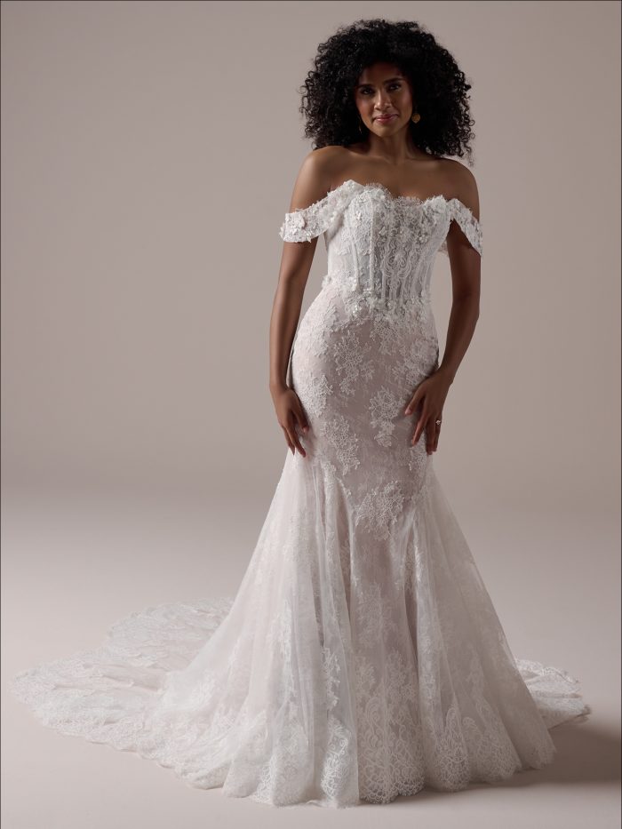 Bride wearing the Takera fit and flare wedding dress featuring off the shoulder lace sleeves, a textured floral bodice, and a softly flared lace skirt with a sweeping train.