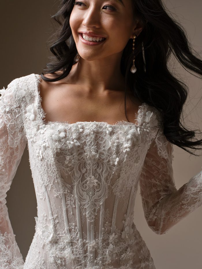 Close-up of the Maggie Sottero Takera Leigh wedding dress showing the lace long sleeves, square neckline, and floral-textured bodice.