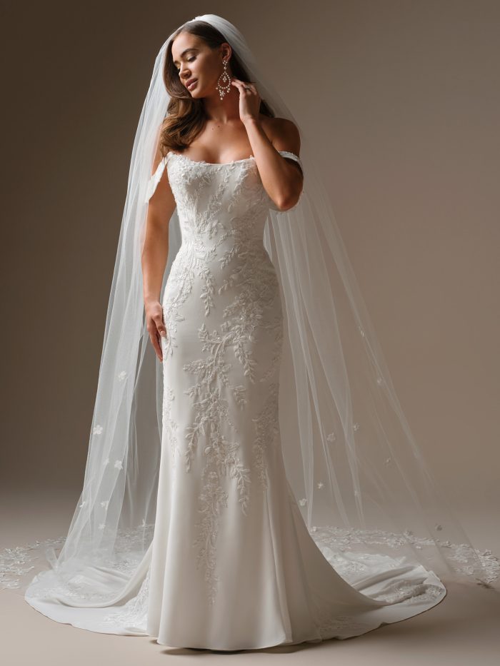 Bride wearing a refined fit-and-flare wedding dress with a strapless cat-eye neckline and embroidered sequin lace. The gown features subtle beading and a long chapel train, styled with a dramatic cathedral veil for a timeless, elegant look.