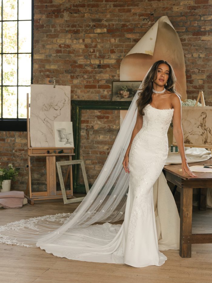 Bride wearing the Thera veil by Maggie Sottero, featuring a cathedral-length tulle veil with scattered floral embellishments paired with a fitted lace sheath gown.