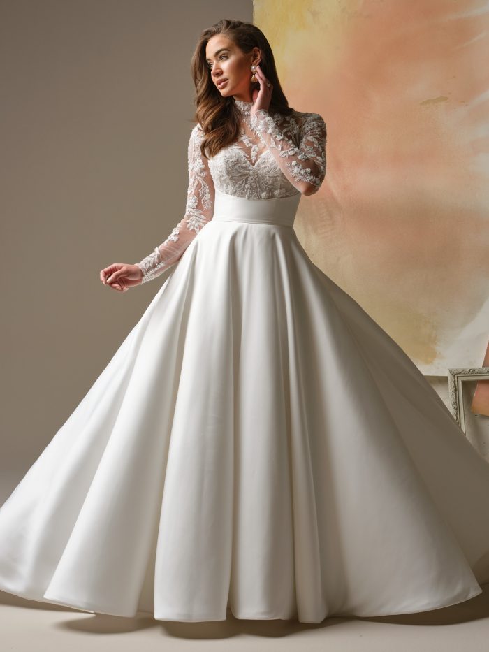 Maggie Sottero Trinity wedding dress featuring a lace high-neck bodice, long illusion sleeves, and a full satin A-line skirt.