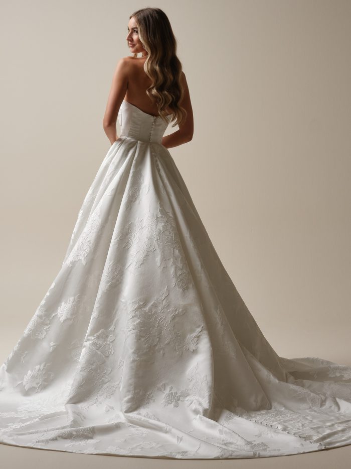 Back view of the Zinaida Marie wedding gown with a full ballgown skirt and chapel train, showcasing embossed floral jacquard fabric and a clean, modern silhouette.
