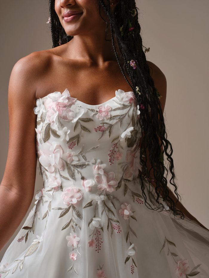 Close-up of Blossom by Rebecca Ingram, featuring a strapless bodice adorned with 3D floral appliqués and pink embroidered leaves on tulle.
