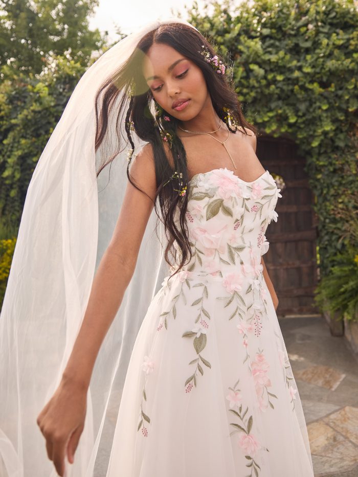 Close-up of the Blossom wedding dress highlighting the strapless bodice with dimensional 3D floral lace, delicate pastel embroidery, and a flowing tulle skirt with soft movement.
