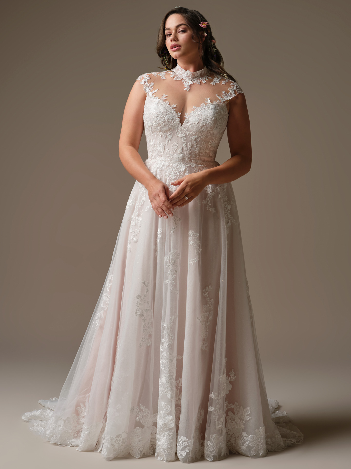 Bride wearing Cody by Rebecca Ingram, a cap-sleeve A-line wedding dress featuring an illusion lace high neckline, fitted lace bodice, soft tulle skirt with floral appliqués, and a flowing chapel-length train.