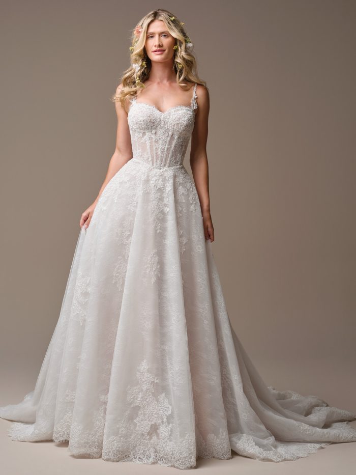 Bride wearing the Esmeralda A-line wedding dress with a sweetheart neckline, sheer lace corset bodice, delicate straps, and a flowing lace skirt with a soft train.