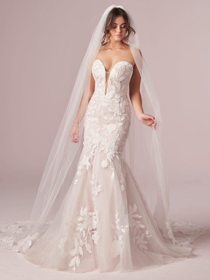 Bride wearing strapless mermaid wedding dress with deep sweetheart neckline, floral lace appliqués, and long tulle veil, highlighting a romantic and figure-flattering silhouette