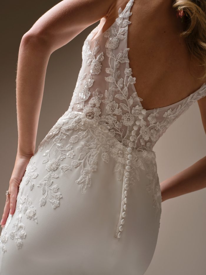 Close-up of the Holly wedding dress featuring an illusion lace bodice with floral appliqués, deep V-back, covered buttons, and smooth crepe skirt.