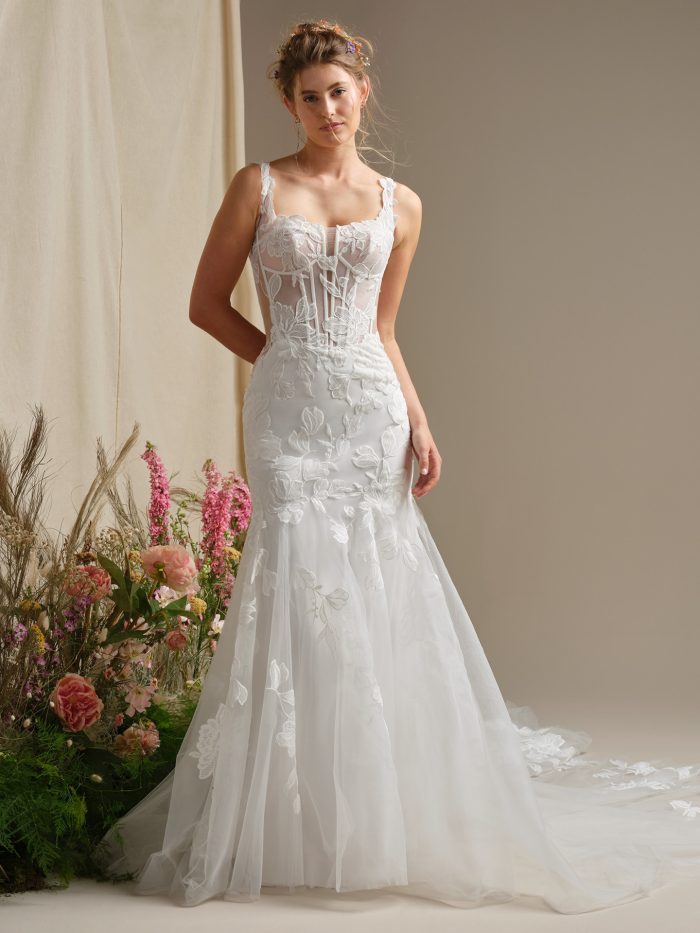 Model wearing a fit-and-flare wedding dress with a plunging square neckline, illusion lace bodice with exposed boning, and floral lace appliqués over a soft tulle skirt and train.