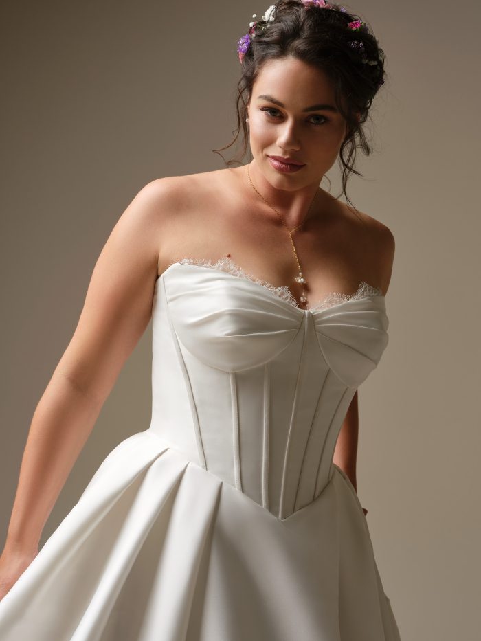 Close-up of Zorina by Rebecca Ingram — plus-size strapless satin ballgown wedding gown featuring structured corset bodice, delicate eyelash lace trim, and sweetheart neckline.