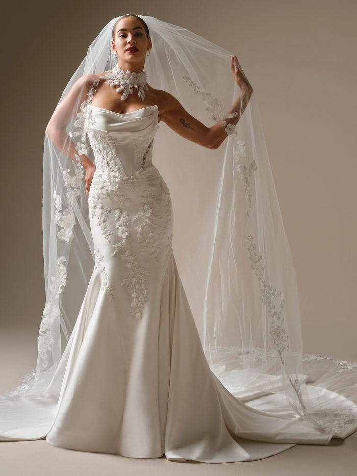 Alt text: “Front view of Sottero and Midgley Burke fit-and-flare wedding dress with draped satin neckline, exposed boning, and beaded floral lace detailing, styled with a cathedral-length embroidered veil.”