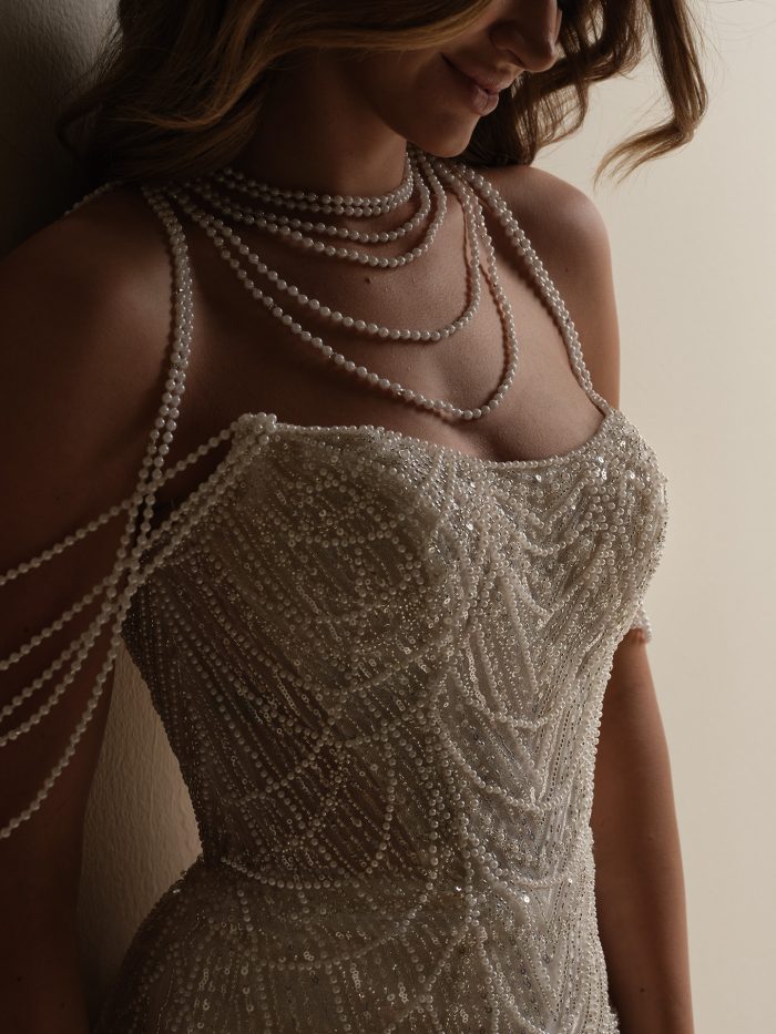 Close-up of Sottero and Midgley Constance wedding dress bodice with hand-beaded geometric patterns and layered pearl accessories draped over the shoulders.